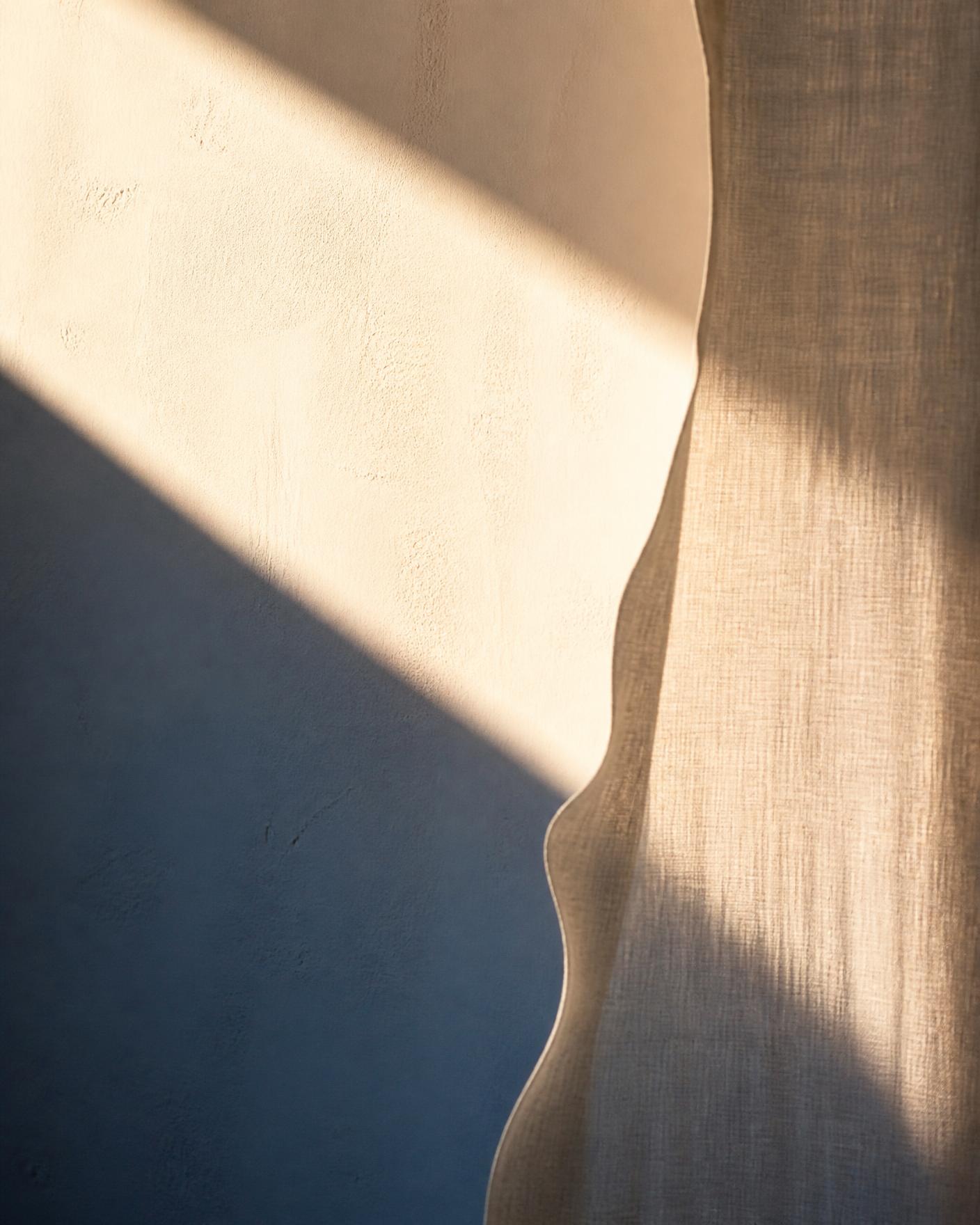 Warm daylight crossing a cream plaster wall and the edge of a linen curtain